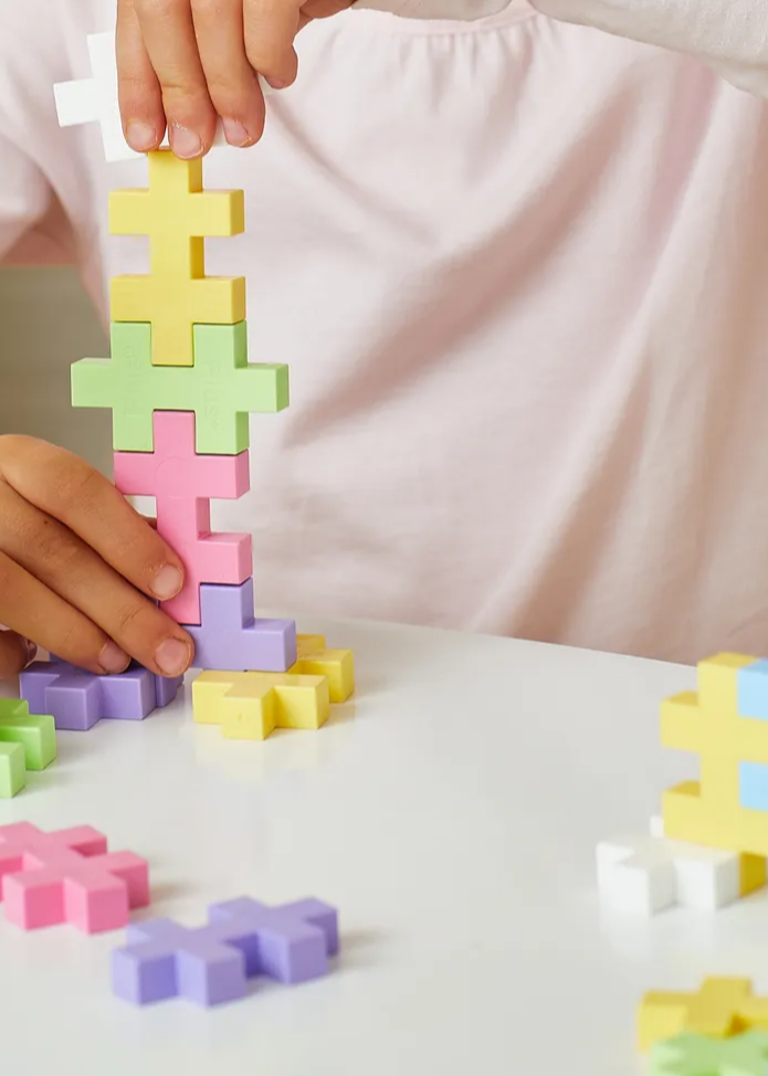 Kinderhanden bouwen een toren met Plus-Plus BIG in pastelkleuren